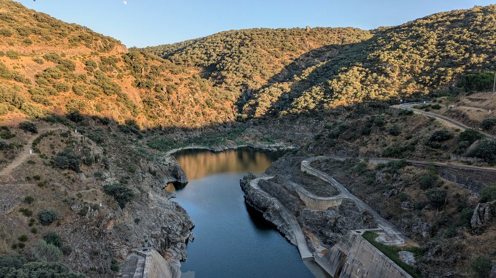 Río encajonado bajo una presa entre laderas de encinas