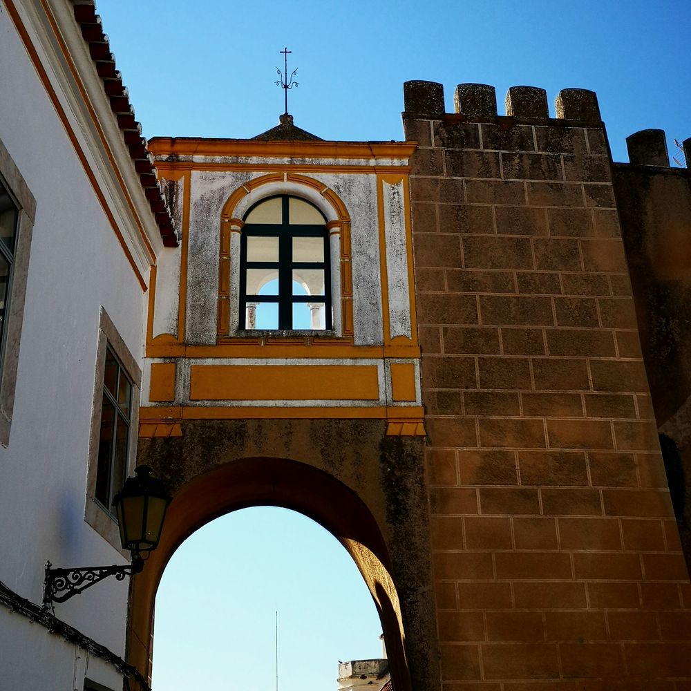 Arco encalado con molduras ocres junto a una muralla almenada